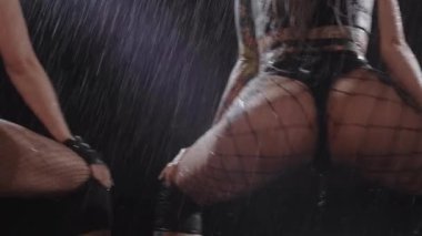 Twerk dancing - women shaking their ass under the rain in dark studio. Mid shot