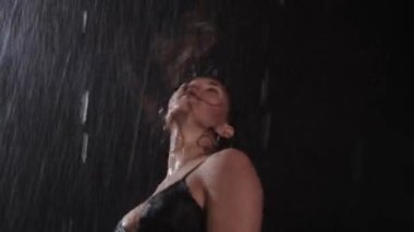 Siyah iç çamaşırlı seksi kadın dansçı başını sallıyor ve yağmurun altında uzun saçlı. Orta çekim
