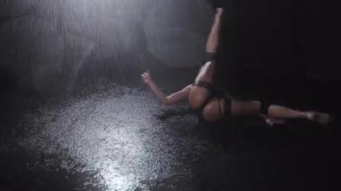 Karanlık stüdyoda, yağmurun altında dans eden siyah iç çamaşırlı, güzel vücutlu seksi bir kadın. Orta çekim