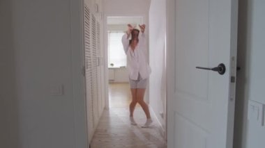 Hafif giysiler içinde gülümseyen genç bir kadın evinin parlak koridorunda dans ediyor. Orta çekim