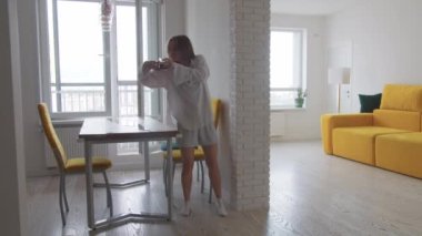 Hafif giysili, heyecanlı genç bir kadın dairesinde kahve içip dans ediyor. Orta çekim