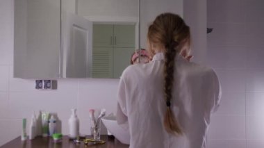 Genç ve güzel bir kadın banyoda aynanın önünde yüz maskesi yapıyor. Orta çekim