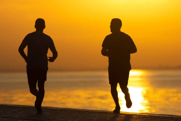 The two men running at the sunrise on river coast, jogging