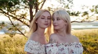 Sahada kameraya poz veren aynı elbiseli iki sarışın kız arkadaş. Orta çekim