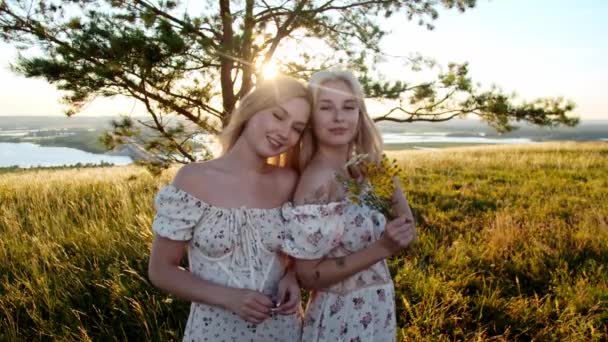 Δύο Χαριτωμένες Ξανθές Κοπέλες Πανομοιότυπα Φορέματα Κρατούν Λουλούδια Και Ποζάρουν — Αρχείο Βίντεο