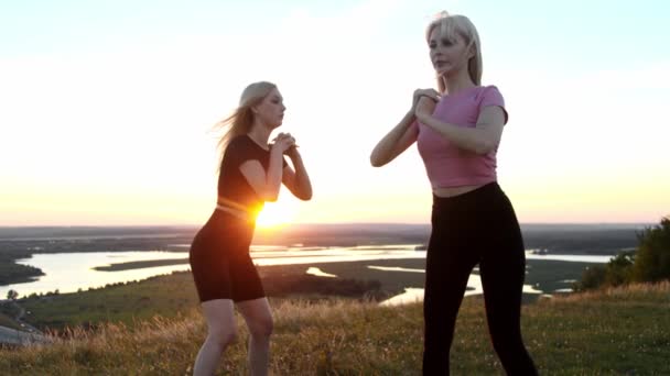 2人の若いスポーツブロンドの女性がフィットネスをして 日没時にフィールドで一緒に不法占拠しています ミッドショット — ストック動画