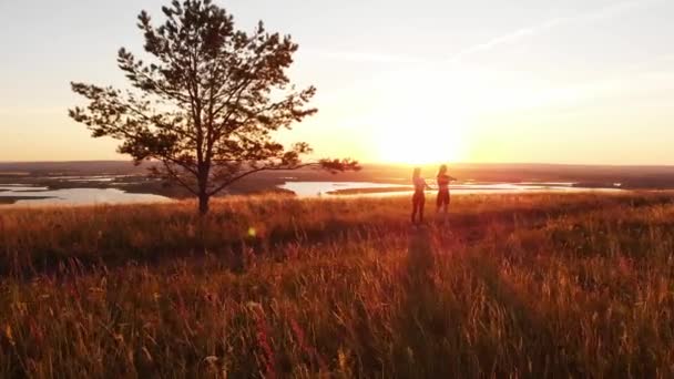 2人の若い痩せた女性が日没時に丘の上に立って体を暖めている 空中風景 — ストック動画