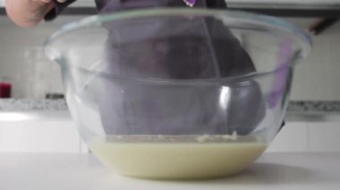 Bir kadın mutfakta hamur işi pişiriyor ve cam kaseye sıvı koyuyor. Orta çekim