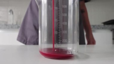 Cam ölçü kabına pasta için kırmızı kaplama koyan bir kadın. Orta çekim