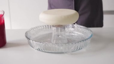 Kadın bir pasta şefi kürsüye pasta koyar ve üzerine kırmızı bir örtü döker. Orta çekim