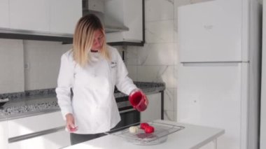 Gülümseyen pasta şefi, kalp şeklinde kekleri parlak kırmızı kaplamayla dolduruyor. Orta çekim