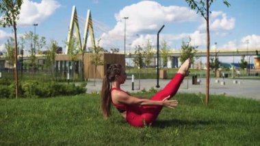 Köprünün yanındaki parkta çimlerde egzersiz yapan kırmızı eşofmanlı spor bir kadın. Orta çekim