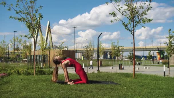 穿着红色训练服的身材魁梧的女人在桥边的公园里练瑜伽 — 图库视频影像