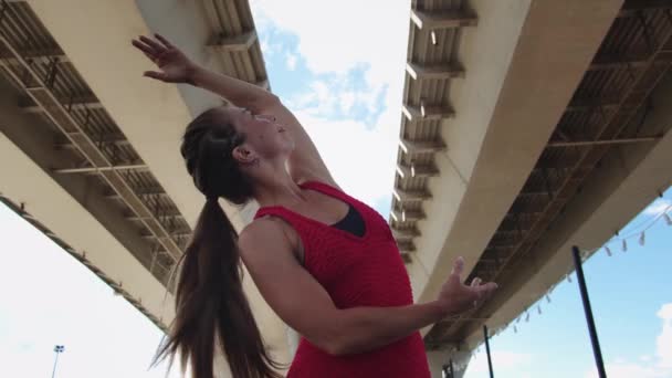 一名身穿红色训练服的成年女子在桥下做简单的练习 — 图库视频影像