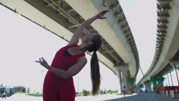一名身穿红色训练服的成年女子在桥下做伸展运动 — 图库视频影像