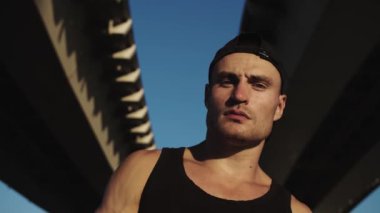 Köprünün altında sakallı çekici kaslı bir adam duruyor. Portre