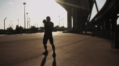 Gün batımında köprünün altında antrenman yapan kaslı bir adam. Orta çekim