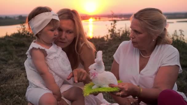只有女性成员的家庭在日落时在山上野餐 祖母向小女孩展示兔子玩具 — 图库视频影像