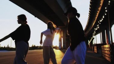 Gün batımında bir köprünün altında hip hop dansı yapan dört sıska genç kadından oluşan bir grup. Orta çekim