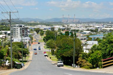 Gladstone, Queensland, Avustralya - 3 Ocak 2018. Gladstone 'un yamaçlık bir mahallesindeki sarp bir caddeden aşağı, binalar, elektrik direkleriyle ve arabalarla Powerhouse' a doğru bakın..