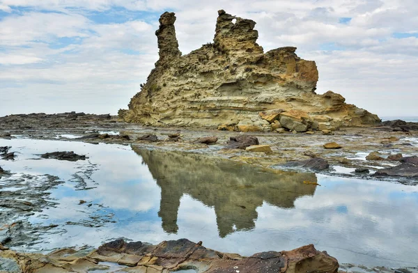 Eagles Nest rock formation in Bunurong Marine and Coastal Park in Victoria, Australia, reflecting in rock pool water.