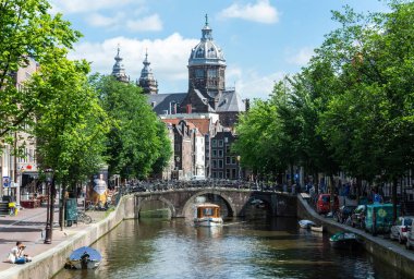 Amsterdam, Hollanda - 22 Haziran 2016. Amsterdam 'ın De Wallen bölgesindeki Oudezijds Voorburgwal kanalı ve caddesi Saint Nicholas Bazilikası' na doğru görünüyor. Teknelerle, arabalarla ve insanlarla manzara.