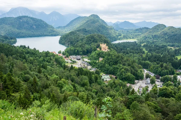 Almanya 'daki Neuschwanstein şatosundan görüntüleme (soldan sağa): saray erişim yolu; önde Hohenschwangau' nun lokalitesine sahip Alpsee; 19. yüzyıl Hohenschwangau Kalesi sağda Schwansee 'nin bulunduğu bir tepenin ardında (batı)).