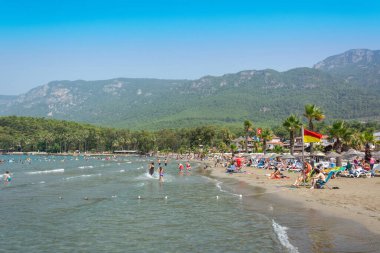 Akyaka, Mugla, Turkey - July 30, 2016. Akyaka beach in the centre of Akyaka village in Mugla province of Turkey, with Sakar mountains in the background, and people.