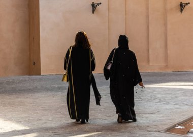 Two unidentifiable Arabic women wearing traditional Islamic black dress  walking away, from the back. One with covered and one with uncovered head.