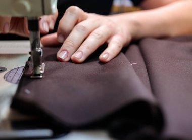 Terzi kadın, elleri atölyede kumaşla çalışıyor.