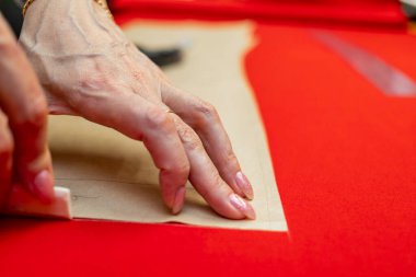 Terzi kadın, elleri atölyede kumaşla çalışıyor.