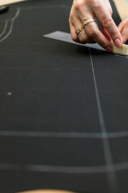 Terzi kadın, elleri atölyede kumaşla çalışıyor.