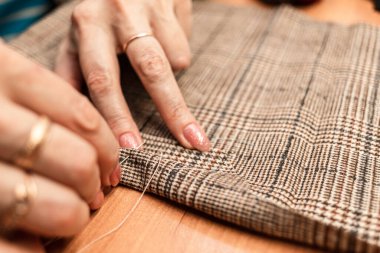 Terzi kadın, elleri atölyede kumaşla çalışıyor.