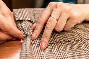 Terzi kadın, elleri atölyede kumaşla çalışıyor.