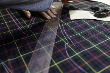 Terzi kadın, elleri atölyede kumaşla çalışıyor.