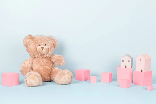 Collezione di giocattoli per bambini. Carino orsacchiotto, cubi di legno rosa e case giocattolo su sfondo azzurro. Vista frontale — Foto Stock