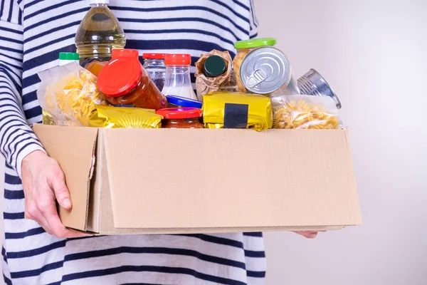 Gönüllü kadın, gıda bağış kutusuyla gıda ürünlerini tutuyor.