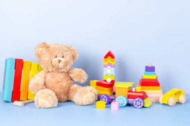 Çocuk oyuncakları koleksiyonu. Oyuncak ayı, tahta tren, gökkuşağı rengi ksilofon ve açık mavi arka planda bebek oyuncakları. Ön görünüm
