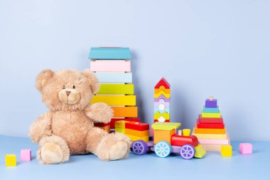Çocuk oyuncakları koleksiyonu. Oyuncak ayı, tahta tren, gökkuşağı rengi ksilofon ve açık mavi arka planda bebek oyuncakları. Ön görünüm
