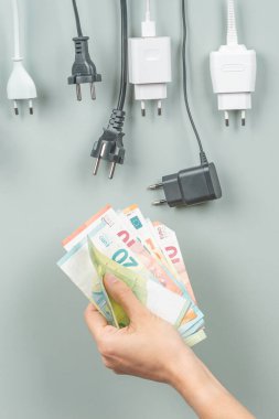 Birçok elektrik kablosu ve Eu fişleri kadının elinde Euro banknotlarıyla asılı. Enerji verimliliği, enerji tüketimi, elektrik maliyeti ve pahalı enerji kavramı