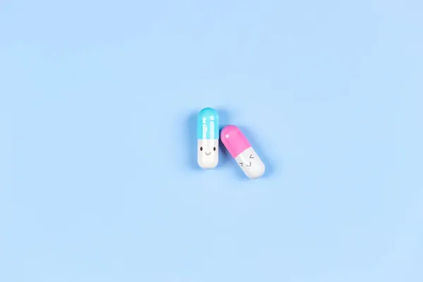 Duas cápsulas de comprimidos de medicamentos coloridos em fundo azul claro. Visão superior, flat lay, espaço de cópia para texto — Fotografia de Stock