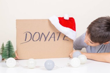 Çocuk elleri, üzerinde yazı olan kahverengi bir karton parçası ve Noel Baba şapkası tutuyor. Noel bağışı, tatil hayır konsepti.