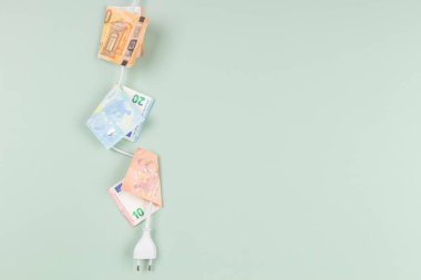Açık yeşil arka planda Euro banknotları asılı elektrik prizi. Enerji verimliliği, enerji tüketimi, elektrik maliyeti ve pahalı enerji kavramı