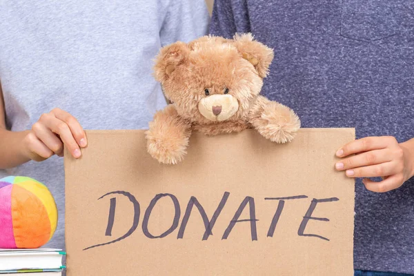 Weihnachtsspende, Weihnachts-Charity-Konzept. Freiwillige Hände halten ein braunes Stück Pappe mit der Aufschrift "Spenden" in der Hand. Kinder sammeln Kleidung, Bücher und Spielzeug — Stockfoto