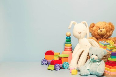 Oyuncak kutusu bebek oyuncaklarıyla dolu. İçinde oyuncak ayı, tüylü ve eğitici ahşap oyuncaklar olan konteynır mavi renkli arka planda. Küçük çocuklar için sevimli oyuncak koleksiyonu. Ön görünüm