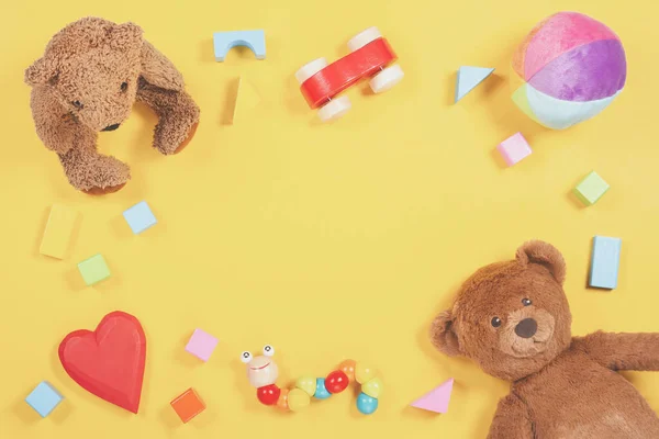 Bambino bambini giocattoli telaio con orsacchiotto, auto giocattolo in legno, mattoni colorati su sfondo giallo. Vista dall'alto — Foto Stock