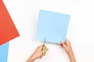 Çocuk sol elinde makasla renkli kağıt kesiyor. Eğitim, öğrenme, kağıt işleri, evde eğlence. Üst görünüm