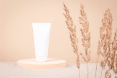 Beyaz kum arka planında, platformda boş plastik kozmetik tüpü. Cilt bakımı, nemlendirici, yüz, vücut kremi, el kremi, mesaj için yeri olan şampuan kutusu. Model yap. Ön görünüm