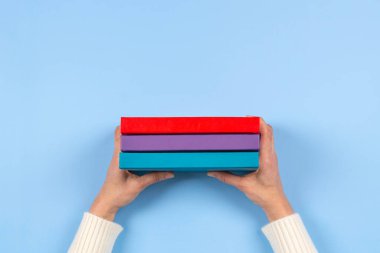 Açık mavi arkaplan üzerinde kitap yığını tutan kadın eller. Eğitim, kendi kendine öğrenme, hobi, evde dinlenme zamanı.