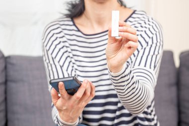 Covid-19 hızlı antijen test cihazı gösteren ve elinde akıllı telefon tutan bir kadın. Test şeridinde kadın elinin negatif test sonuçlarını gösteren yakın çekimi